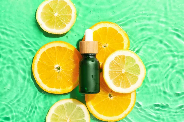 Bottle with vitamin C serum and slices of citrus fruits in water on color background