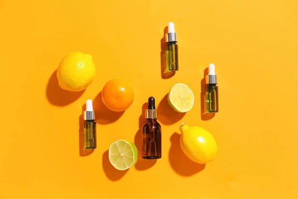 Bottles of vitamin C serum and citrus fruits on color background