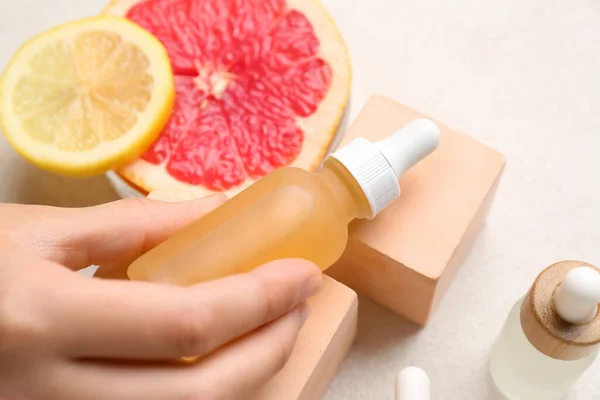 Female hand with bottle of vitamin C serum on light background, closeup