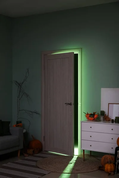 Door with glowing green light in dark living room decorated for Halloween