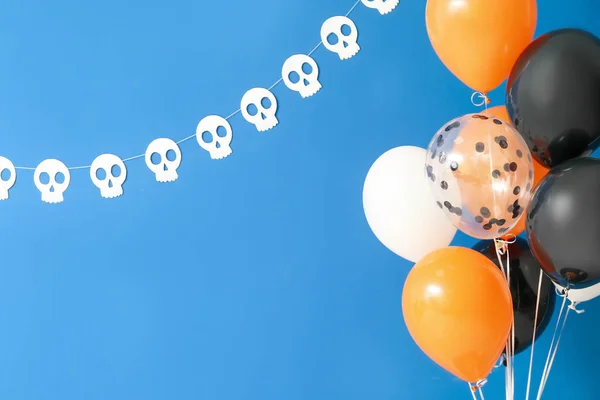 Halloween balloons and paper human skulls hanging on blue wall