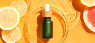 Turuncu arka planda bir şişe turunçgil yağı ve meyve dilimleri.