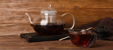 Ahşap zeminde bir bardak puer çayı ve çaydanlık.