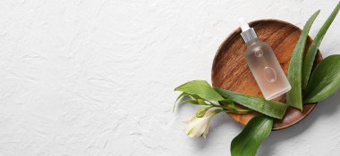 Kozmetik serumu, çiçek ve yeşil yapraklı ahşap plaka. Arka planda yazı için yer var, üst görünüm için.