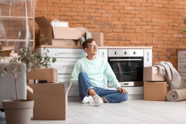 Genç adam taşınma gününde mutfakta oturuyor.