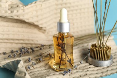 Mavi arka planda gerekli yağ, kenzan ve kağıt içeren kozmetik damlası şişesi, yakın plan.