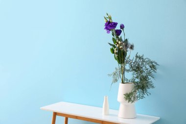 Mavi duvarın yanındaki masada güzel ikebana vazoları var.