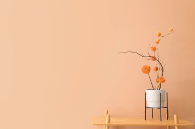 Bej duvarın yanındaki rafta güzel ikebana otları var.