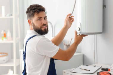 Erkek tesisatçı banyoda kazan tamir ediyor.