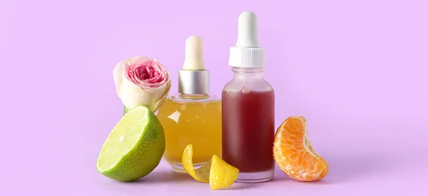 Bottles of citrus essential oil on lilac background
