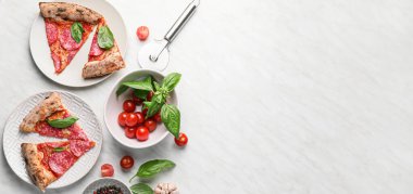 Lezzetli pizza dilimleri, domates ve fesleğen açık arkaplanda ve metin için yer var.