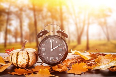 Alarm clock, pumpkin and autumn leaves on table outdoors