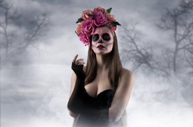 Meksika Ölüler Günü 'nde (El Dia de Muertos) ormanda boyalı yüzü ve şeker kafatası olan genç bir kadın.