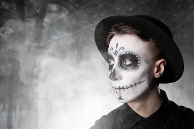 Ormanda Meksika Ölüler Günü 'nde (El Dia de Muertos) yüzünde boyalı kafatası olan genç bir adam.