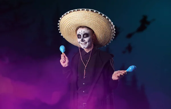 Young man with painted skull on his face and maracas at night. Celebration of Mexico's Day of the Dead (El Dia de Muertos)