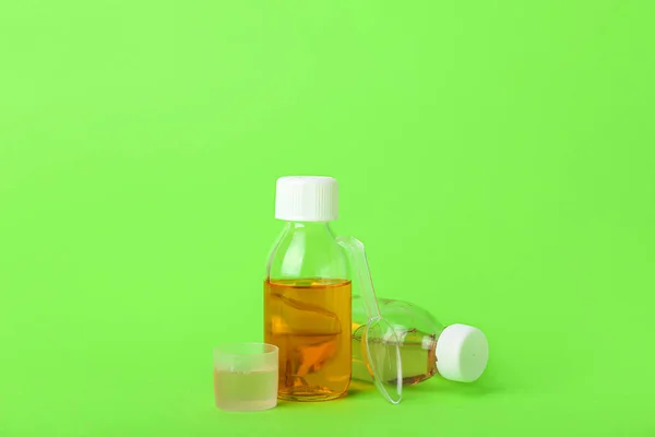 Bottles of cough syrup, cup and spoon on green background