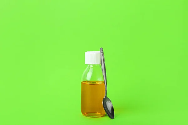 Bottle of cough syrup and spoon on green background