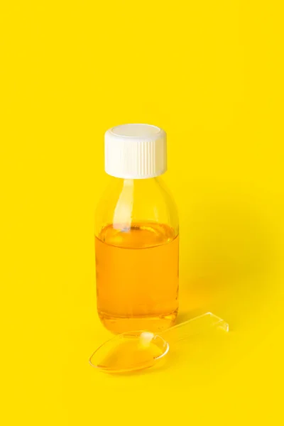 Bottle and spoon of cough syrup on yellow background