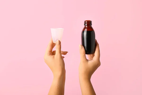 Woman with bottle of cough syrup and cup on pink background