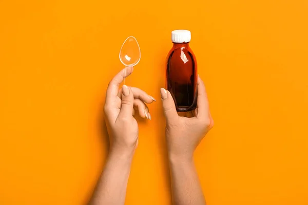 Woman with bottle of cough syrup and spoon on orange background