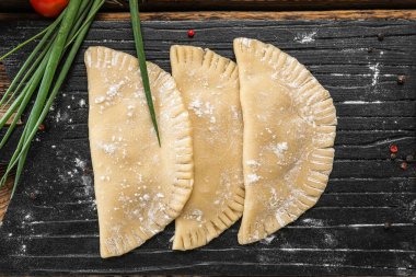 Ahşap zemin üzerinde çiğ chebureks ve yeşil soğan olan tahta