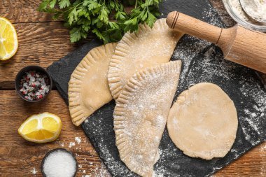 Tahtada çiğ chebureks, merdane, limon, maydanoz ve ahşap arka planda baharatlar var.