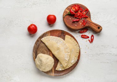 Beyaz arka planda çiğ chebureks, hamur, tahta ve sebze tabağı