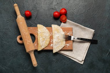 Koyu arka planda çiğ chebureks, çatal, merdane ve domatesli tahta.