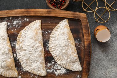 Siyah zemin üzerinde çiğ cheburekler ve yumurta kabukları olan tahta