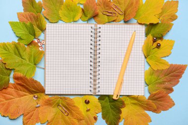 Mavi arkaplanda açık defter, kalem ve sonbahar yaprakları