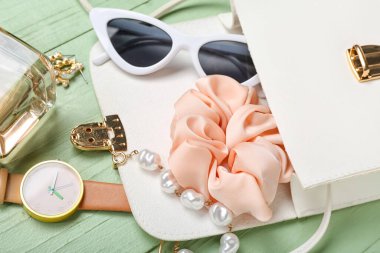 Yeşil ahşap arka planda farklı aksesuarlarla açılmış kadın çantası.