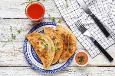 Lezzetli chebureks tabağı, bir bardak domates suyu ve ahşap arka planda sos.