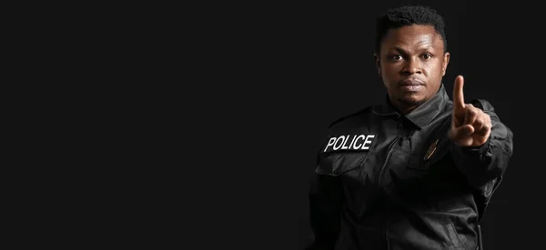 African-American police officer pointing at viewer on dark background with space for text
