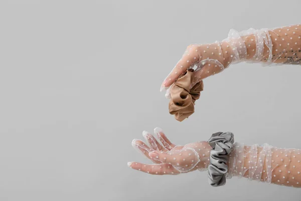 Woman in elegant gloves holding silk scrunchies on light background, closeup