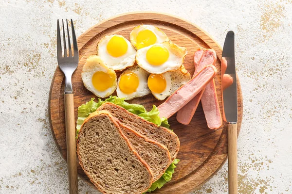 Hafif arka planda kızarmış bıldırcın yumurtası, ekmek ve sosisli ahşap tahta pano, yakın plan.