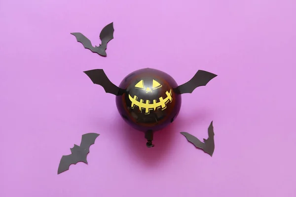 Funny Halloween balloon and paper bats on color background