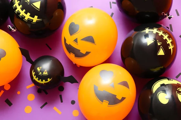 Funny Halloween balloons and confetti on lilac background