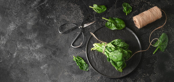 Plate with fresh spinach leaves, scissors and thread on dark background with space for text