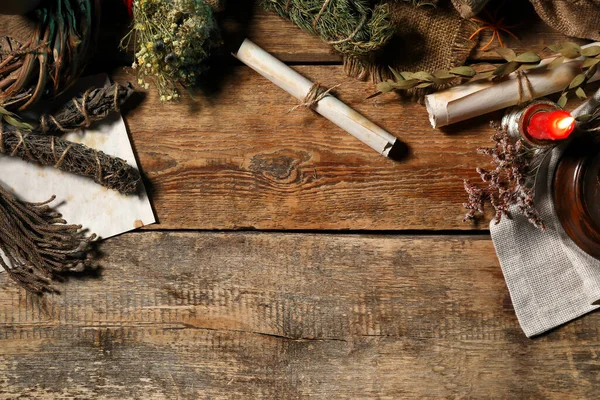 Ancient scrolls, burning candle and dry herbs on wooden table