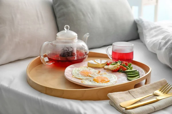 Wooden tray with tasty breakfast on bed