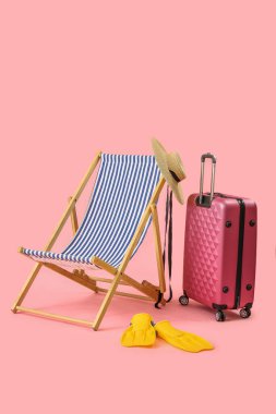 Güverte sandalyesi, bavul ve pembe arka planda plaj aksesuarları.