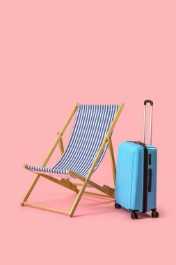 Plaj sandalyesi ve pembe arka planda bavul.