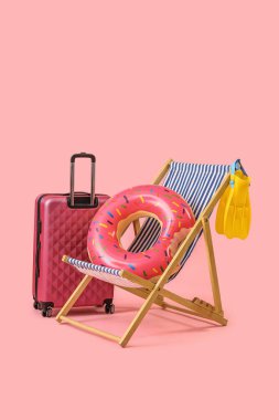 Güverte sandalyesi, bavul ve pembe arka planda plaj aksesuarları.