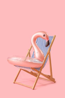 Plaj sandalyesi ve pembe arka planda şişme yüzük.