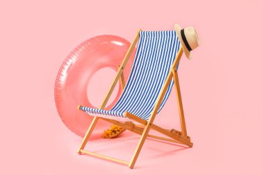 Plaj sandalyesi, şapka ve pembe arka planda şişme yüzük.