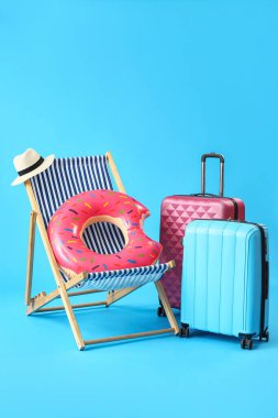 Güverte sandalyesi, bavullar ve açık mavi arka planda plaj aksesuarları.