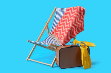 Güverte koltuğu, bavul ve açık mavi arka planda plaj aksesuarları.