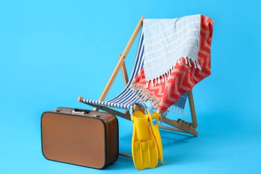 Güverte koltuğu, bavul ve açık mavi arka planda plaj aksesuarları.