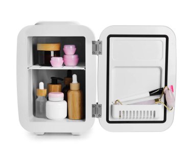 Beyaz arka planda doğal kozmetik ürünleri, fırça ve masaj aleti olan küçük buzdolabı