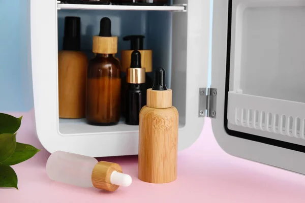 Small refrigerator with natural cosmetics on pink table near blue wall